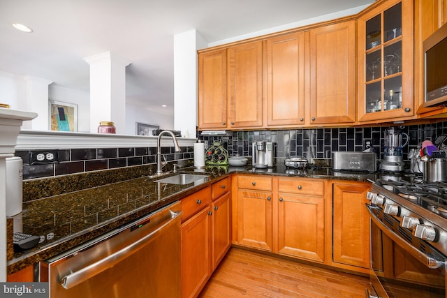 kitchen with light wood-type flooring, backsplash, dark stone counters, stainless steel appliances, and sink