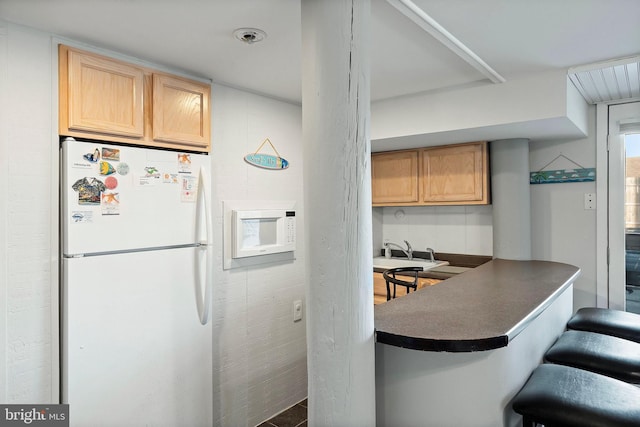 kitchen with a breakfast bar, light brown cabinetry, dark countertops, freestanding refrigerator, and a peninsula