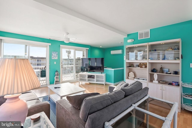 living area with visible vents, a ceiling fan, a wall mounted AC, wood finished floors, and baseboards