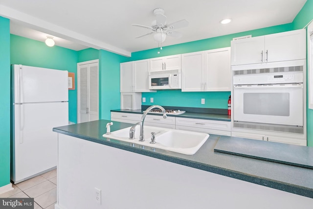 kitchen featuring dark countertops, light tile patterned floors, white appliances, white cabinetry, and a sink