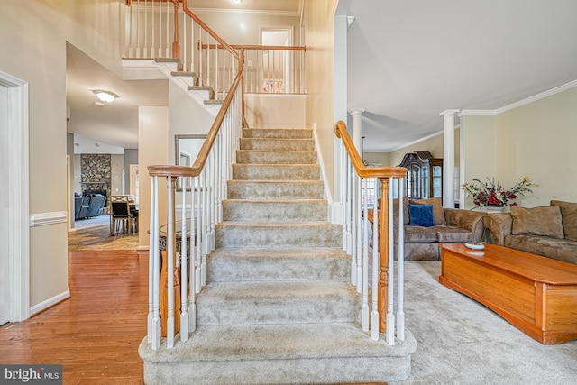 staircase with ornate columns, ornamental molding, a high ceiling, and hardwood / wood-style flooring