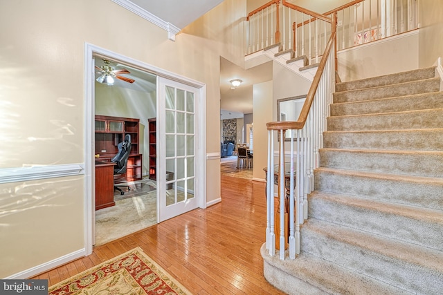 stairs with ceiling fan, wood-type flooring, crown molding, and french doors