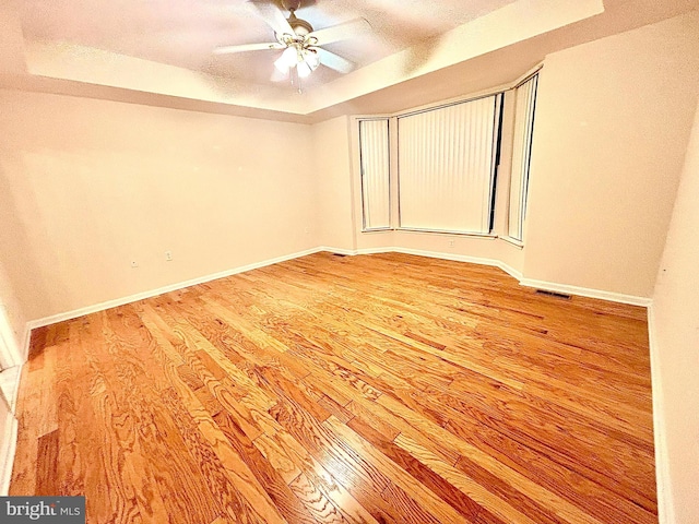 unfurnished room with hardwood / wood-style floors, a textured ceiling, a tray ceiling, and ceiling fan