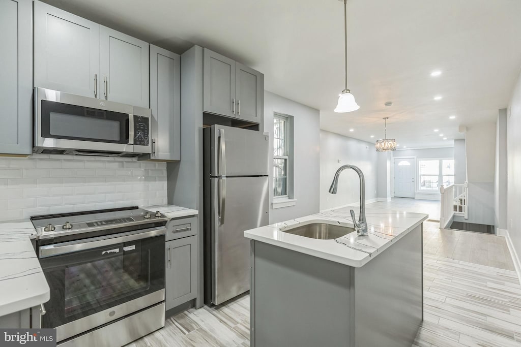 kitchen featuring sink, stainless steel appliances, light hardwood / wood-style flooring, decorative light fixtures, and a kitchen island with sink