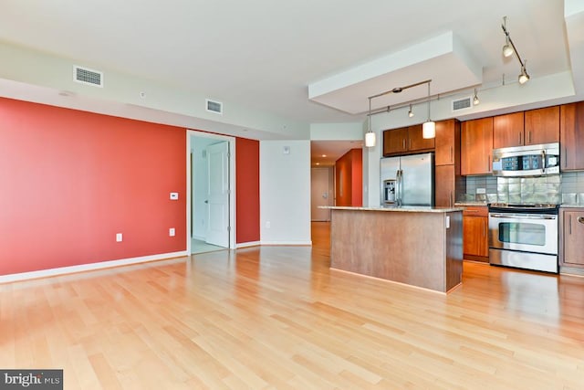 kitchen with hanging light fixtures, rail lighting, light wood-type flooring, appliances with stainless steel finishes, and tasteful backsplash