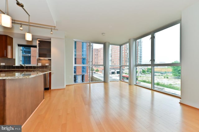 kitchen featuring sink, stone countertops, a wall of windows, light hardwood / wood-style floors, and hanging light fixtures