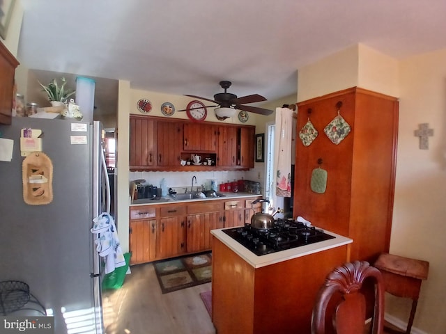 kitchen featuring stainless steel refrigerator, sink, kitchen peninsula, black gas stovetop, and light wood-type flooring