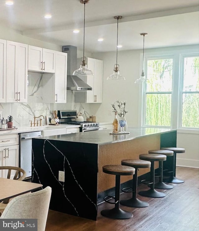 kitchen featuring white cabinets, wall chimney exhaust hood, decorative light fixtures, a kitchen island, and stainless steel appliances