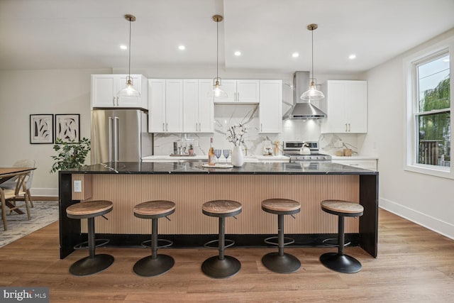 kitchen featuring white cabinetry, a center island, wall chimney range hood, appliances with stainless steel finishes, and light wood-type flooring