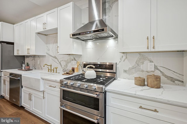 kitchen with decorative backsplash, wall chimney exhaust hood, stainless steel appliances, sink, and white cabinets