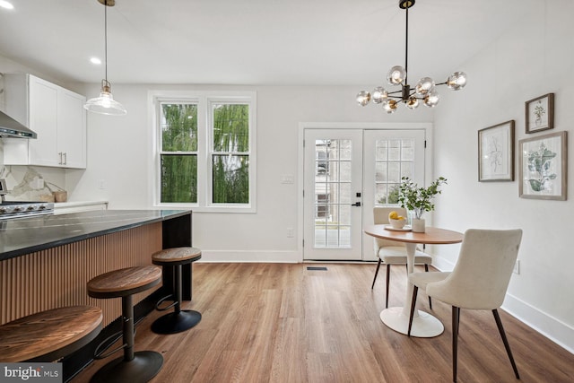 dining area featuring french doors, light wood-type flooring, and an inviting chandelier