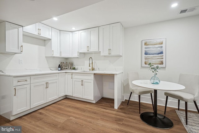 kitchen with white cabinets, light stone counters, light wood-type flooring, and sink