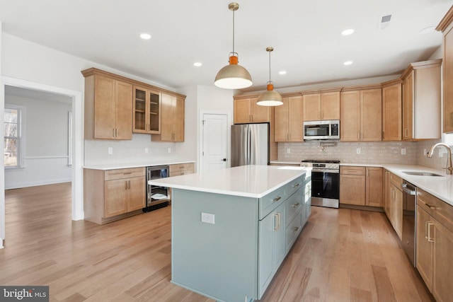 kitchen with wine cooler, sink, hanging light fixtures, appliances with stainless steel finishes, and a kitchen island