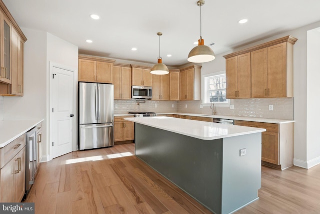 kitchen featuring sink, decorative light fixtures, a kitchen island, stainless steel appliances, and light hardwood / wood-style floors