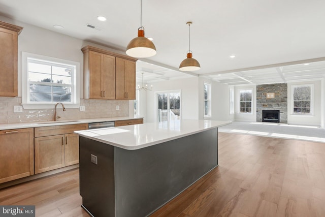 kitchen with a kitchen island, sink, backsplash, hanging light fixtures, and light hardwood / wood-style flooring