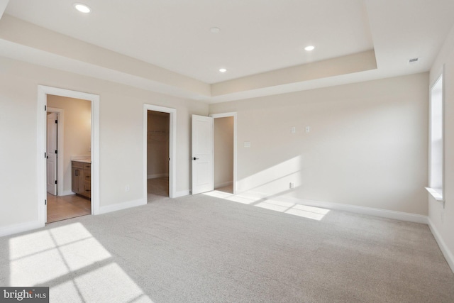 unfurnished bedroom featuring a spacious closet, light colored carpet, and a tray ceiling