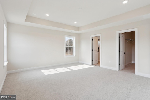 unfurnished bedroom featuring light carpet, a closet, a spacious closet, and a raised ceiling