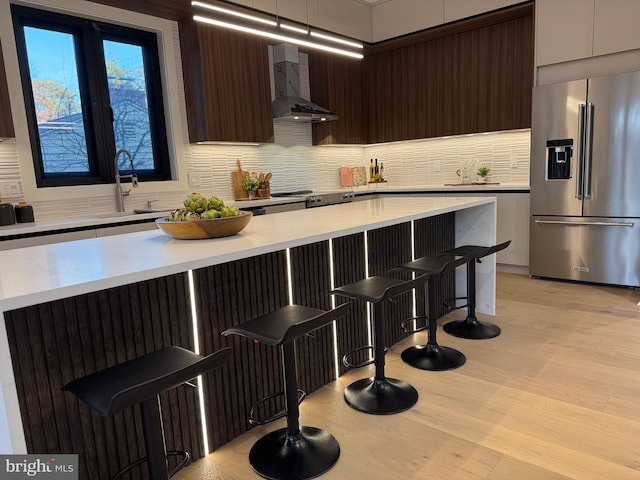 kitchen featuring a kitchen bar, decorative backsplash, wall chimney exhaust hood, and appliances with stainless steel finishes