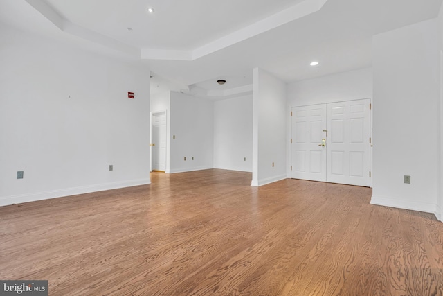 empty room with light wood-type flooring and a tray ceiling