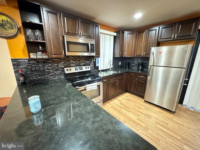 kitchen with sink, appliances with stainless steel finishes, tasteful backsplash, dark brown cabinets, and light hardwood / wood-style floors