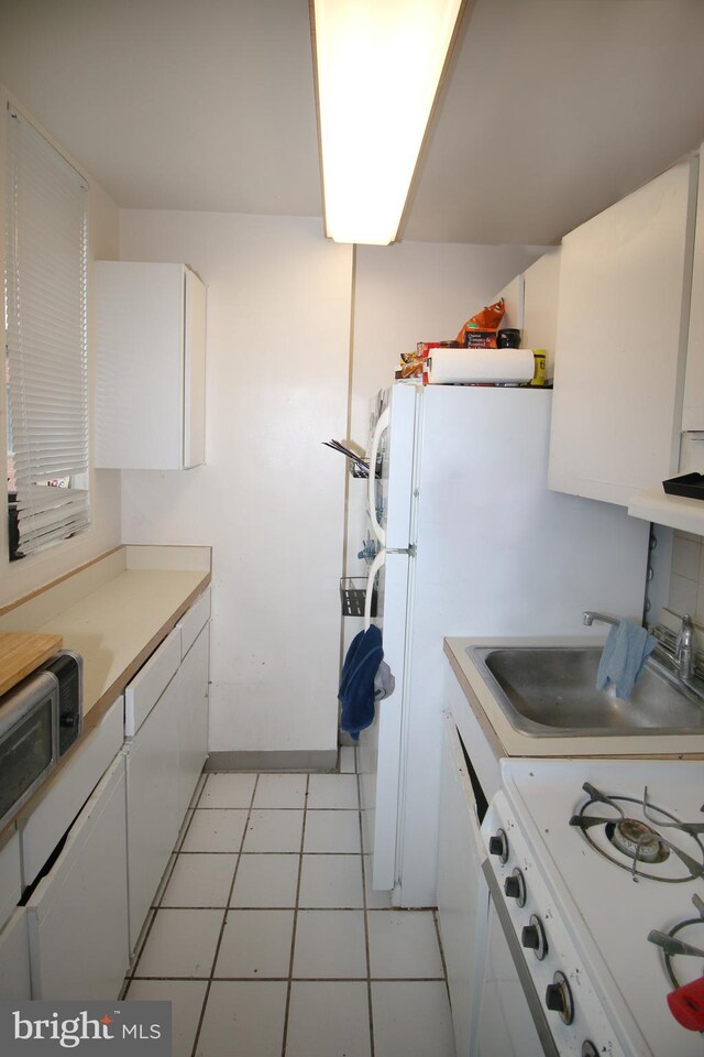 kitchen with white cabinets, sink, light tile patterned floors, and white stove