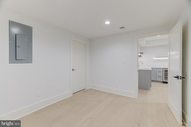 unfurnished room featuring sink, wine cooler, electric panel, and light hardwood / wood-style flooring