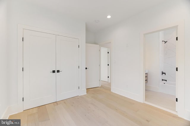 unfurnished bedroom featuring ensuite bath, light hardwood / wood-style floors, and a closet