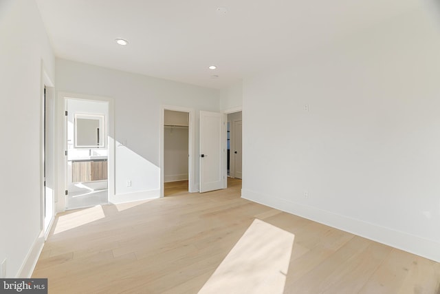 unfurnished bedroom featuring a walk in closet, ensuite bathroom, light hardwood / wood-style floors, and a closet