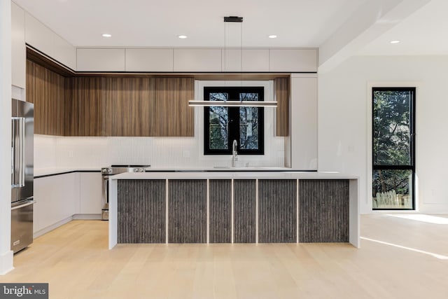 kitchen with light hardwood / wood-style flooring, appliances with stainless steel finishes, hanging light fixtures, backsplash, and white cabinets