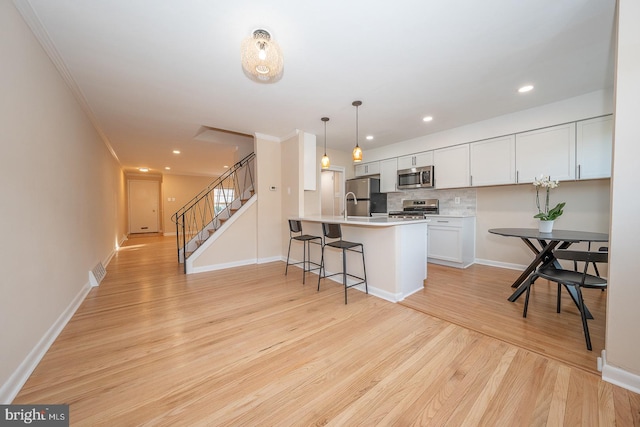 kitchen with hanging light fixtures, light hardwood / wood-style flooring, kitchen peninsula, white cabinets, and appliances with stainless steel finishes