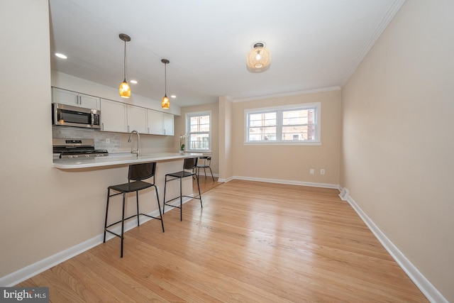 kitchen featuring appliances with stainless steel finishes, light wood-type flooring, a breakfast bar, white cabinets, and ornamental molding