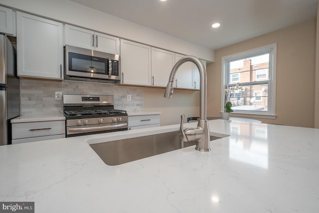 kitchen with decorative backsplash, light stone counters, sink, and appliances with stainless steel finishes