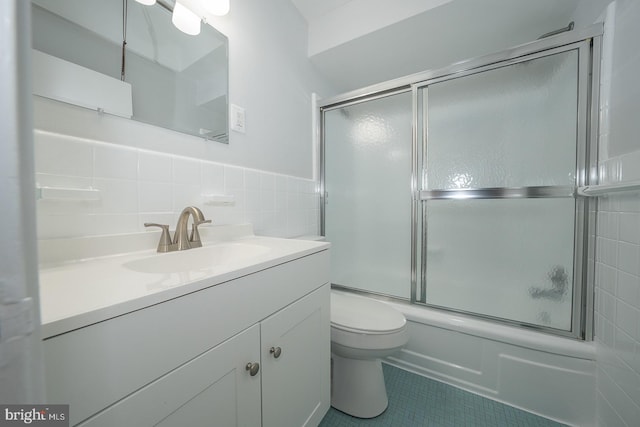 full bathroom with vanity, shower / bath combination with glass door, tile patterned floors, toilet, and tile walls