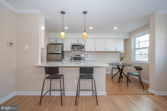 kitchen with white cabinets, a kitchen bar, stainless steel appliances, and light hardwood / wood-style flooring