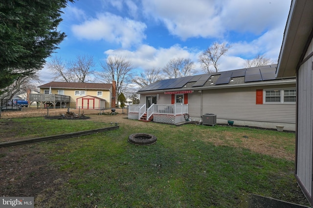 back of property with solar panels, central air condition unit, a storage shed, a wooden deck, and an outdoor fire pit