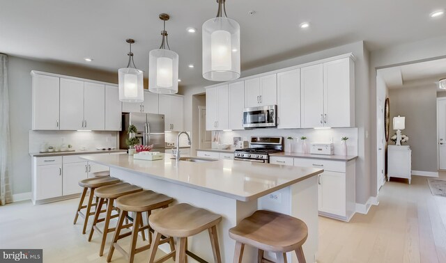 kitchen with sink, light hardwood / wood-style flooring, a kitchen island with sink, white cabinets, and appliances with stainless steel finishes