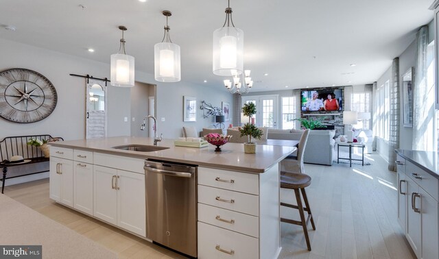 kitchen with a barn door, decorative light fixtures, stainless steel dishwasher, and a center island with sink