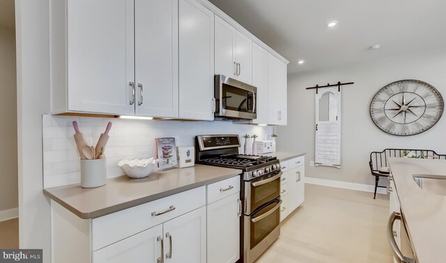 kitchen with tasteful backsplash, a barn door, white cabinets, and stainless steel appliances