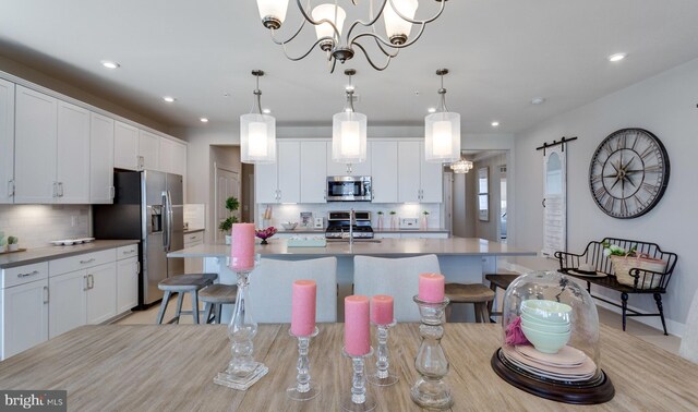 kitchen with decorative light fixtures, white cabinetry, an island with sink, and appliances with stainless steel finishes