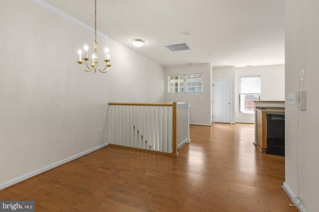 empty room featuring crown molding, an inviting chandelier, and hardwood / wood-style flooring