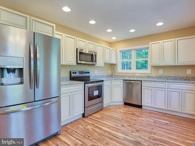 kitchen with sink, stainless steel appliances, light stone counters, light hardwood / wood-style floors, and white cabinets