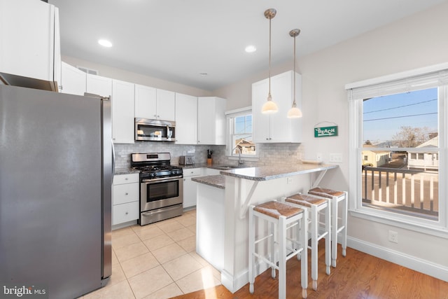 kitchen with white cabinetry, a kitchen breakfast bar, kitchen peninsula, pendant lighting, and appliances with stainless steel finishes