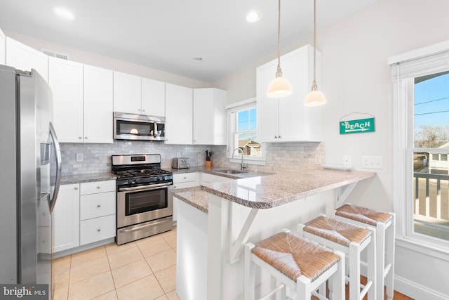 kitchen with kitchen peninsula, appliances with stainless steel finishes, sink, pendant lighting, and a breakfast bar area