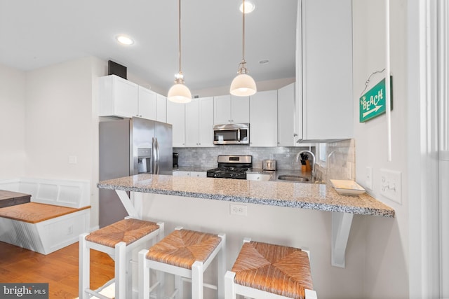 kitchen with white cabinets, sink, light wood-type flooring, appliances with stainless steel finishes, and kitchen peninsula