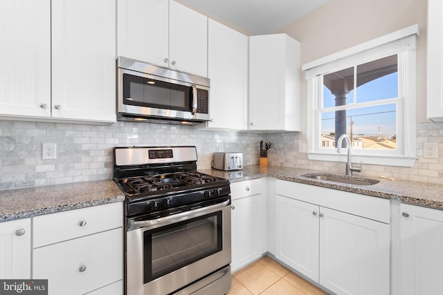 kitchen with light stone countertops, tasteful backsplash, stainless steel appliances, sink, and white cabinetry