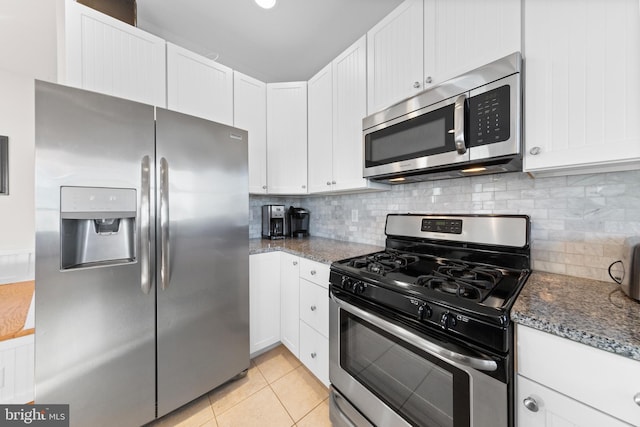 kitchen featuring dark stone countertops, white cabinets, light tile patterned floors, and appliances with stainless steel finishes