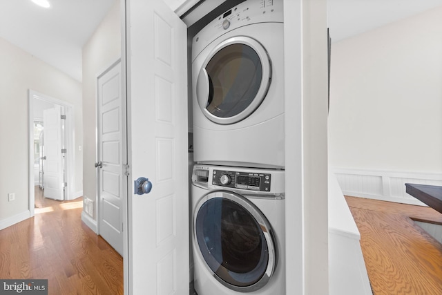 clothes washing area with hardwood / wood-style floors and stacked washing maching and dryer