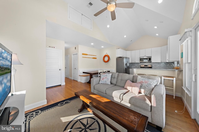 living room with ceiling fan, light hardwood / wood-style flooring, high vaulted ceiling, and sink