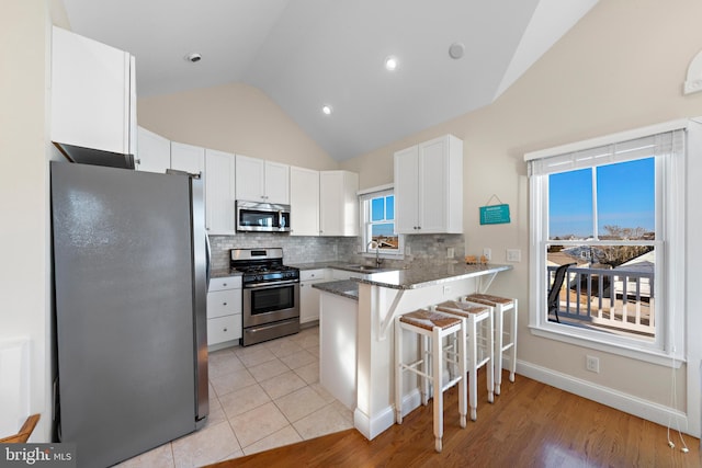 kitchen featuring kitchen peninsula, appliances with stainless steel finishes, a kitchen bar, dark stone countertops, and white cabinetry