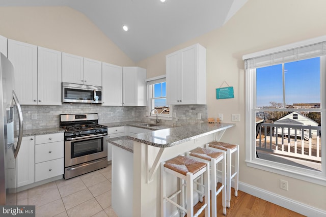 kitchen featuring white cabinetry, sink, kitchen peninsula, a kitchen bar, and appliances with stainless steel finishes